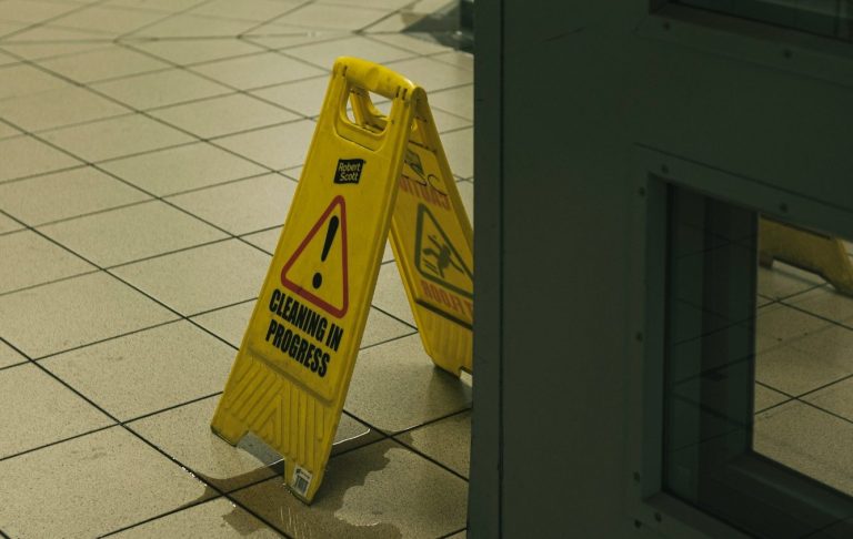 Ein gelbes Warnschild mit der Aufschrift 'Reinigung im Gange' steht auf einem nassen Boden.